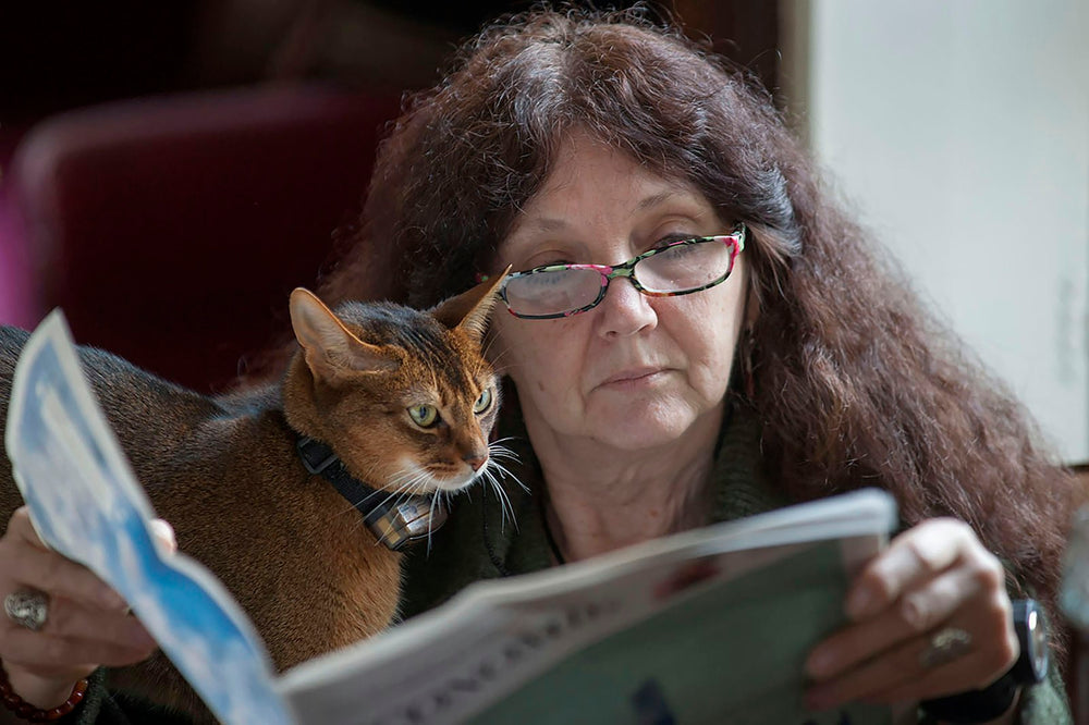 Une femme lit le journal avec son chat sur l'épaule
